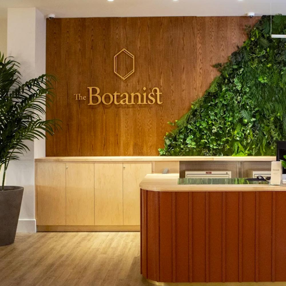 Reception space showcasing The Botanist branding, warm wood finishes, and a living green wall design